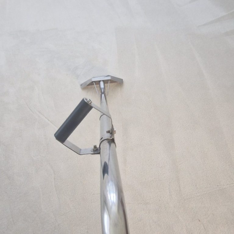 A close-up of a chrome carpet cleaning tool on a light surface.